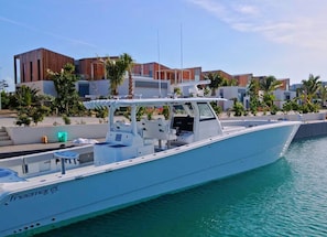 A white yacht docked at a marina with modern buildings and palm trees in the background.
