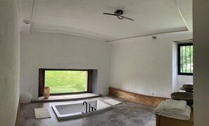 A bathroom with a large bathtub, a window with a view of greenery, and a ceiling fan. - Renovated villa with 2 swimming pools and a hot tub (Latronquière)