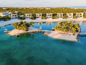 Un complex turístic amb diverses cases modernes, una piscina central i una zona de platja.