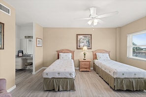 A bedroom with two beds, a desk, a chair, a ceiling fan, and a window. - Spacious 3BR/3BA Condo | Private Beach Access (Satellite Beach)