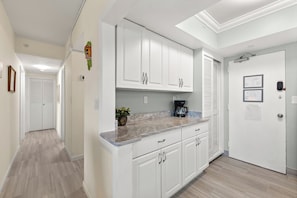 A modern kitchen with white cabinetry, a granite countertop, and a coffee maker. - Spacious 3BR/3BA Condo | Private Beach Access (Satellite Beach)
