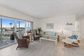 A spacious living room with a balcony, wicker furniture, a sofa with decorative pillows, and a painting on the wall. - Spacious 3BR/3BA Condo | Private Beach Access (Satellite Beach)