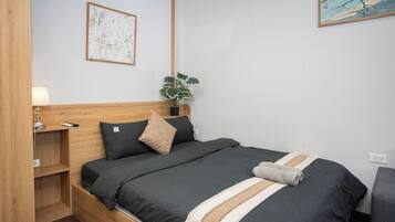 Un lit bien fait, avec une couette de couleur foncée, une tête de lit en bois et une table de chevet sur laquelle se trouve une lampe.