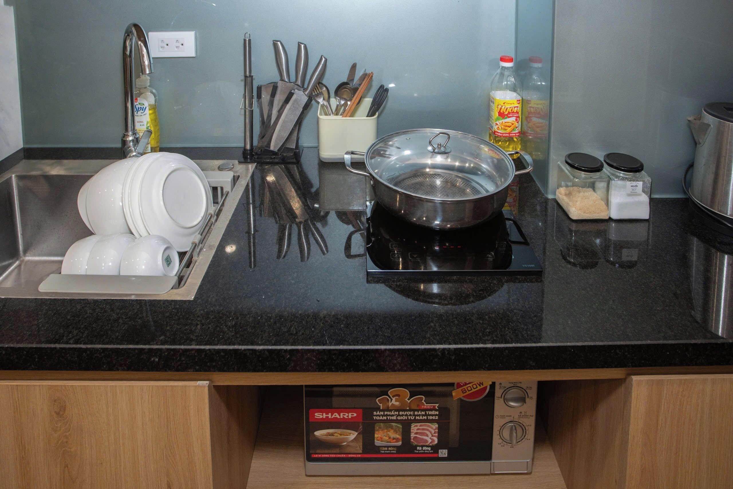 A kitchen with a sink, dish rack, utensils, a pot on the stove, and a box of Sharp brand rice cooker.