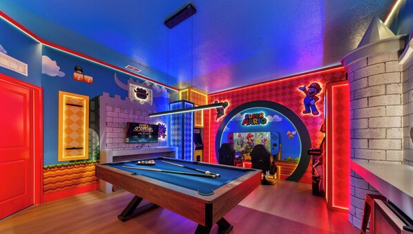 Ein Zimmer mit Billardtisch, Nintendo Switch und einer Wand im Stil von Super Mario.