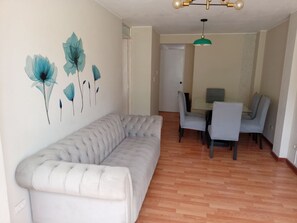 A living room with a sofa, a dining table with chairs, and a wall with floral artwork. - 2-bedroom, 2-bathroom apartment, 15 minutes from the airport (Lima)