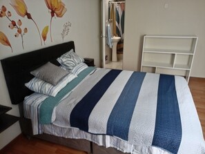 A bedroom with a bed, pillows, a bedside table, a nightstand, a mirror, a wardrobe, and a white shelving unit. - 2-bedroom, 2-bathroom apartment, 15 minutes from the airport (Lima)