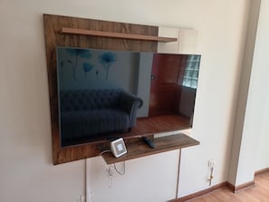 A modern living room with a mounted flat-screen TV, a sofa, and a wooden shelf. - 2-Bedroom, 2-Bathroom Apartment, 15 Minutes from the Airport (Lima)