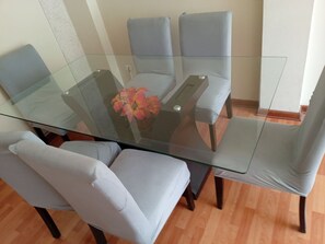A glass-top dining table with four grey chairs, a vase with flowers, and a wooden floor. - 2-Bedroom, 2-Bathroom Apartment, 15 Minutes from the Airport (Lima)