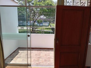 A room with a sliding glass door leading to a balcony with a stone floor and a view of a park and buildings. - 2-bedroom, 2-bathroom apartment, 15 minutes from the airport (Lima)