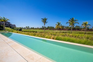 Ein Swimmingpool mit einer klaren, blauen Wasserlinie, umgeben von einer Rasenfläche mit Palmen und einem Golfplatz im Hintergrund.