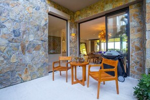Un muro esterno in pietra, un patio con mobili in legno e un barbecue.