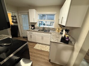 A compact kitchen with white cabinets, a granite countertop, a built-in stove, and a window with blinds. - La hermosa casa del lago. St Cloud. Florida (St. Cloud)