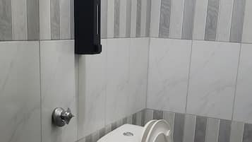 A bathroom with a toilet, a hand dryer, and a wall-mounted soap dispenser.