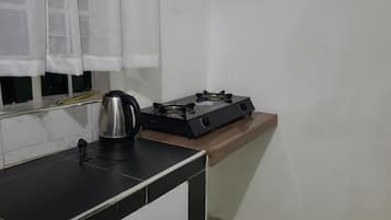 A kitchen with a gas stove, a kettle, and a window with curtains.