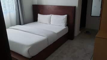 A bed with a wooden headboard, white bedding, and a pair of slippers on the floor.