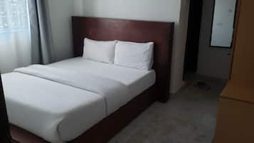 A hotel room with a bed, a wooden headboard, a white mattress, and a tiled floor.