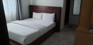 A hotel room with a bed, a wooden headboard, a white mattress, and a tiled floor. - Micah Global Accommodations (Nairobi)