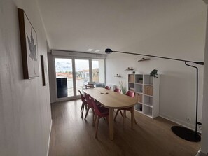 A modern dining area with a wooden table and chairs, a large window with a view, and a floor lamp. - Appartement rénové, résidence avec piscine (BISCARROSSE)