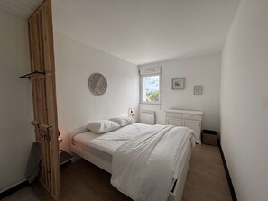 A bedroom with a bed, a window, a bedside table, and a dresser. - Appartement rénové, résidence avec piscine (BISCARROSSE)