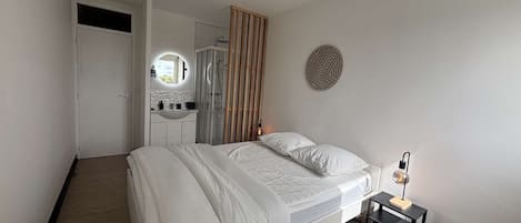 A bedroom with a bed, a bedside table, a mirror, and a shower area.