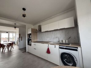 A modern kitchen with white cabinetry, a built-in oven, a washing machine, and a dining area with a table and chairs. - Appartement rénové, résidence avec piscine (BISCARROSSE)