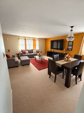 A living room with a sofa set, a coffee table, and a dining table with chairs. - Luxury 3BR Queens Getaway; Smart TVs, A/C & Near JFK, LGA and UBS Arena (St Albans)