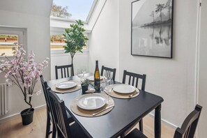 A dining table set with plates, glasses, and a bottle, surrounded by chairs, with a framed picture on the wall and a plant on the table. - Modern Stay near Kahlenberg & Vineyards (Wien)