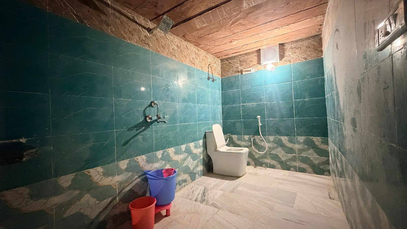 A bathroom with a toilet, a shower, and a blue bucket.
