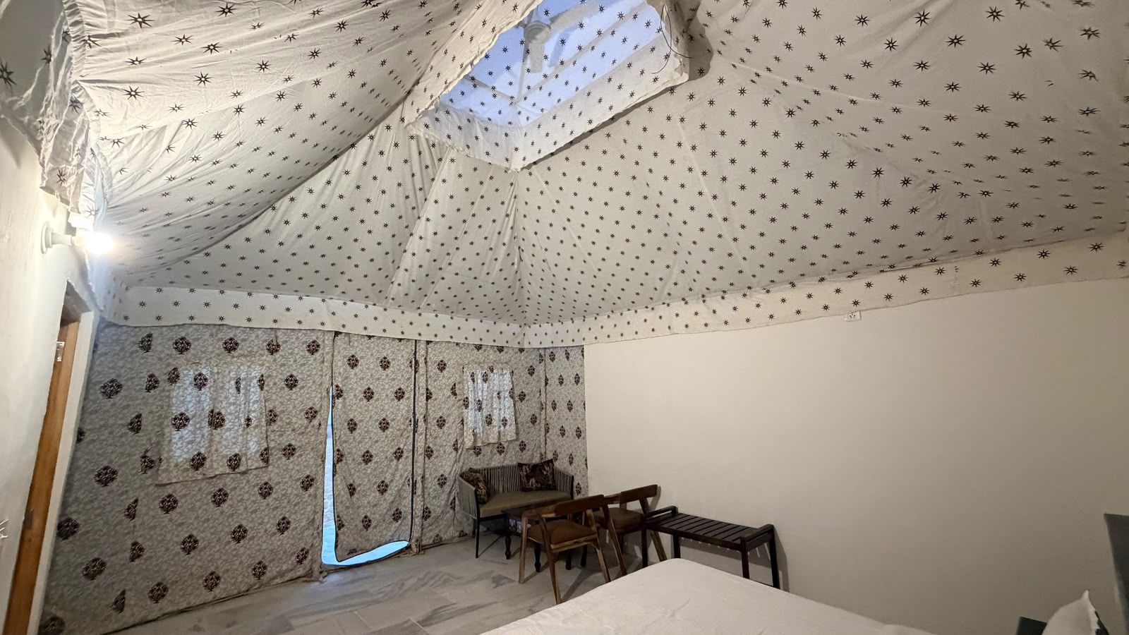 A room with a bed, a table, and chairs. There is a window with curtains.