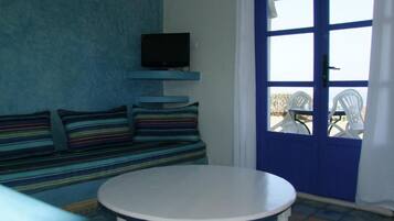 Una habitación con puerta azul, televisor montado en la pared, un sofá a rayas y una mesa redonda.
