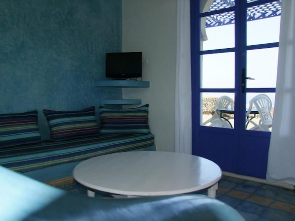 A room with a blue door, a television mounted on the wall, a striped sofa, and a round table.