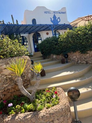 A hotel with a blue roof and a sign that reads 'HOTEL RESTAURANT.' There are steps leading up to the entrance, and the building is surrounded by greenery.