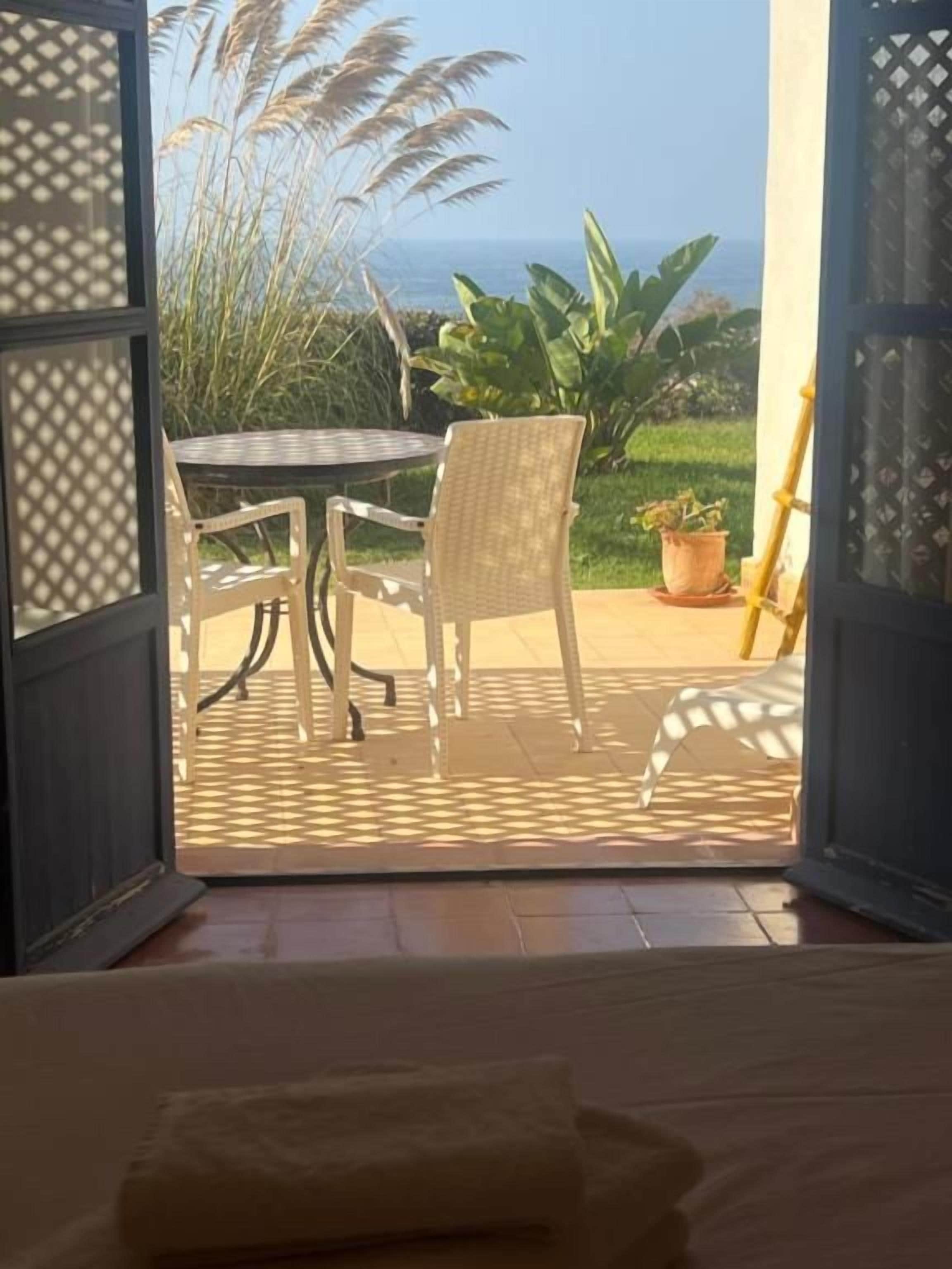 An open door leading to a patio with a table and chairs, a potted plant, and a view of the sea.