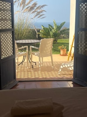 An open door leading to a patio with a table and chairs, a potted plant, and a view of the sea.