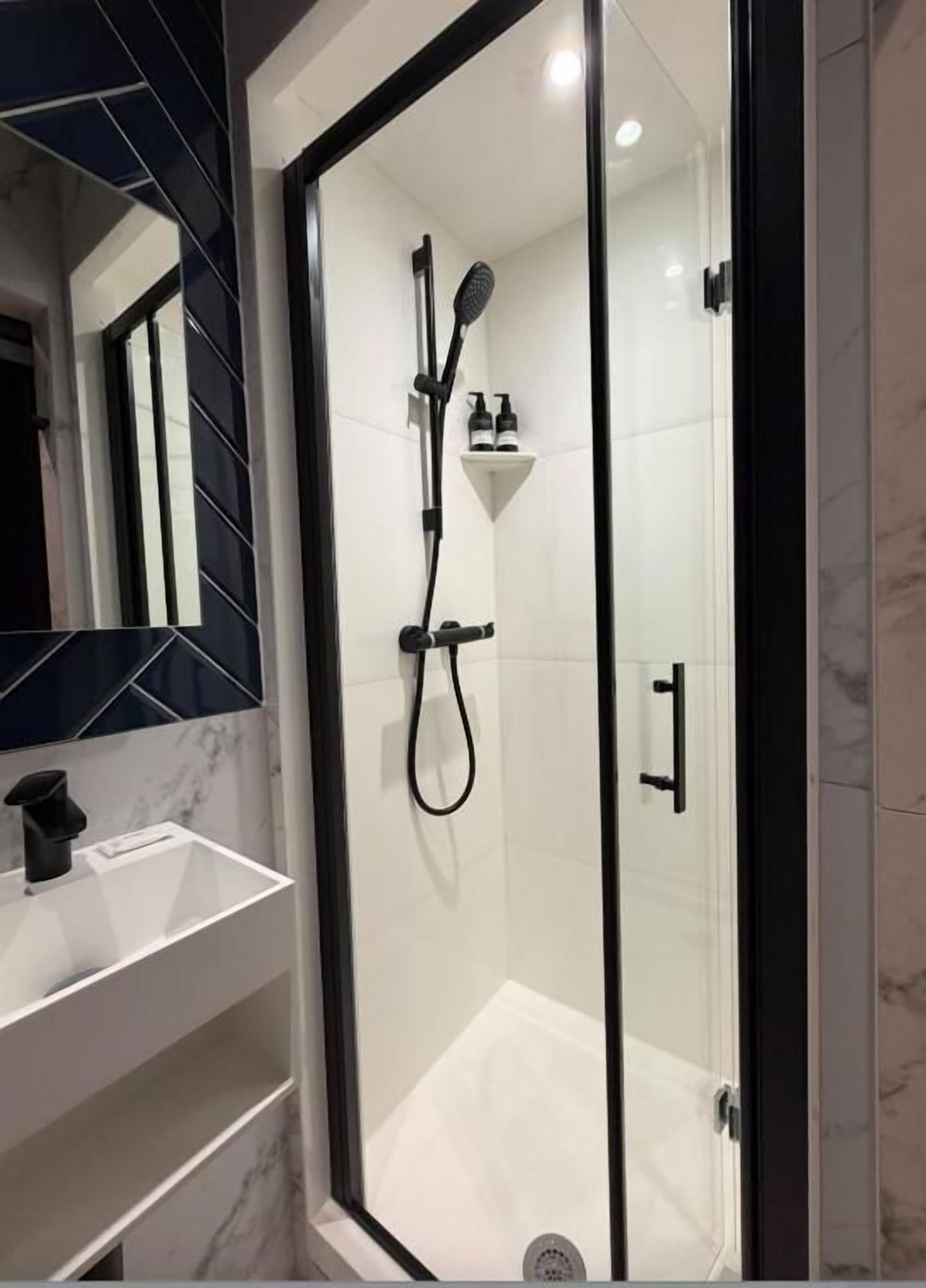 Un baño moderno con ducha envuelta en vidrio, lavamanos blanco y salpicadero de mármol.