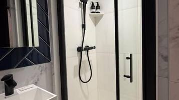 Un baño moderno con ducha envuelta en vidrio, lavamanos blanco y salpicadero de mármol.