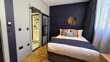 A modern hotel room with a large bed, a round mirror, and a view of a bathroom.