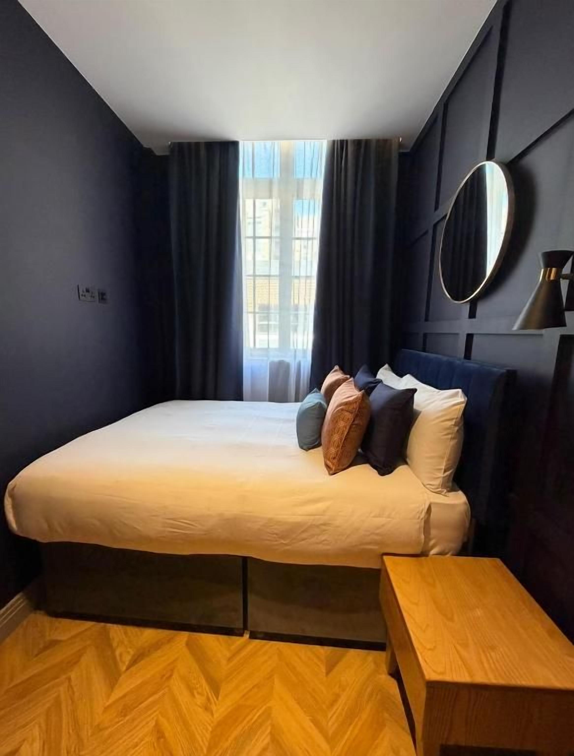 Un dormitorio con una cama, una mesita de noche, un espejo y una ventana con cortinas.