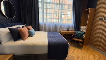 Camera d'albergo con un ampio letto, pavimento in legno, una scrivania e una finestra vista edifici.