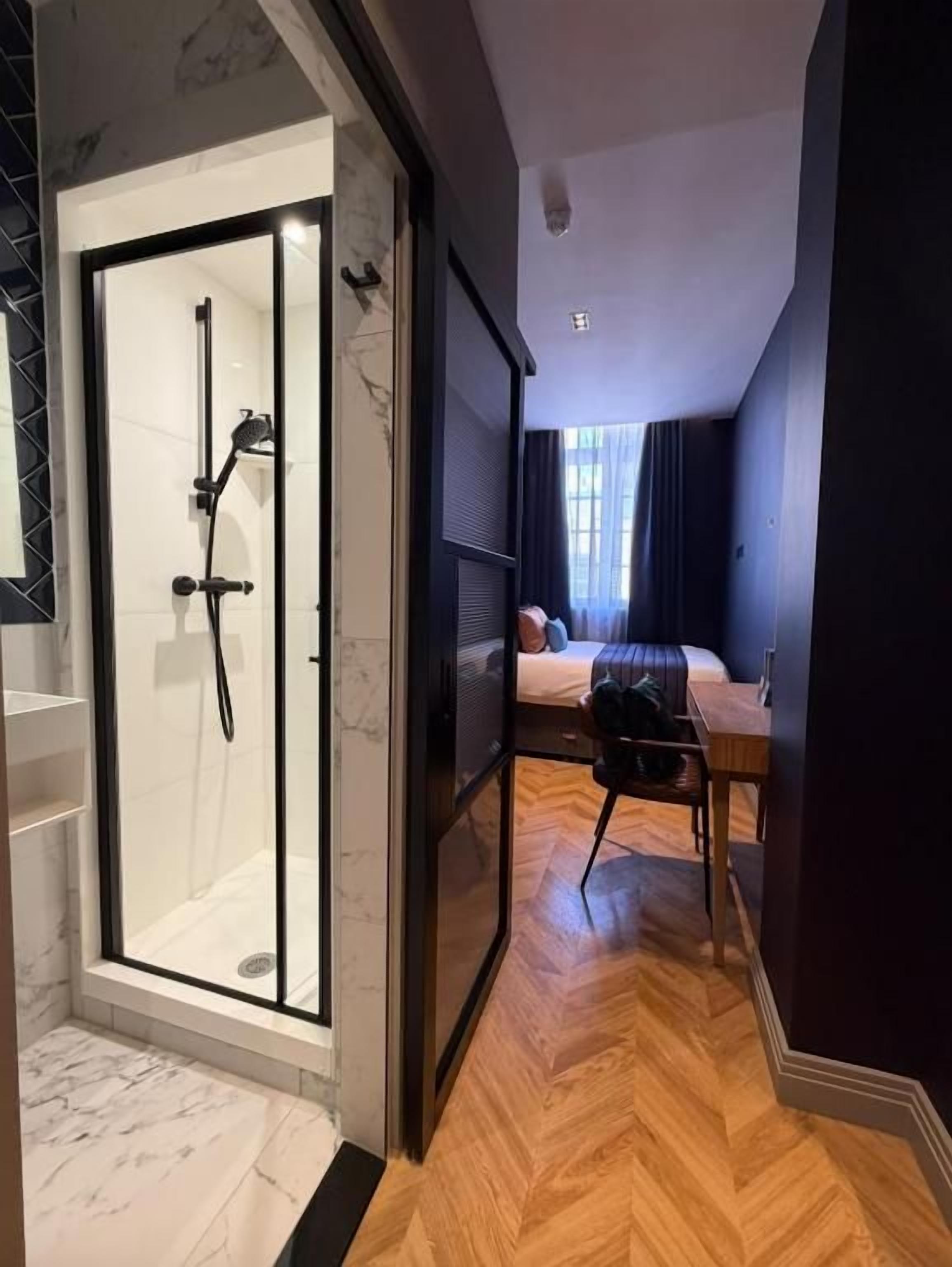 Une salle de bain moderne dotée d’une douche à parois de verre et d’un plancher en bois menant à une chambre à coucher avec un lit et une table de chevet.