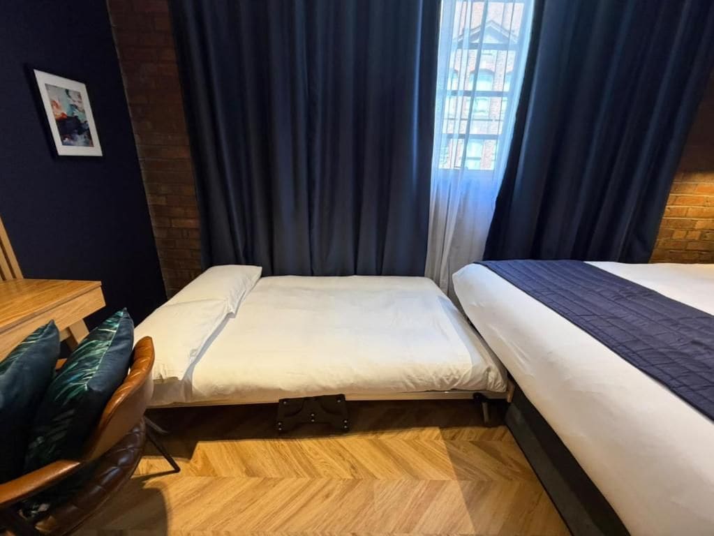 Een kamer met twee bedden, een houten vloer, een raam met gordijnen en een kleine tafel met een stoel.