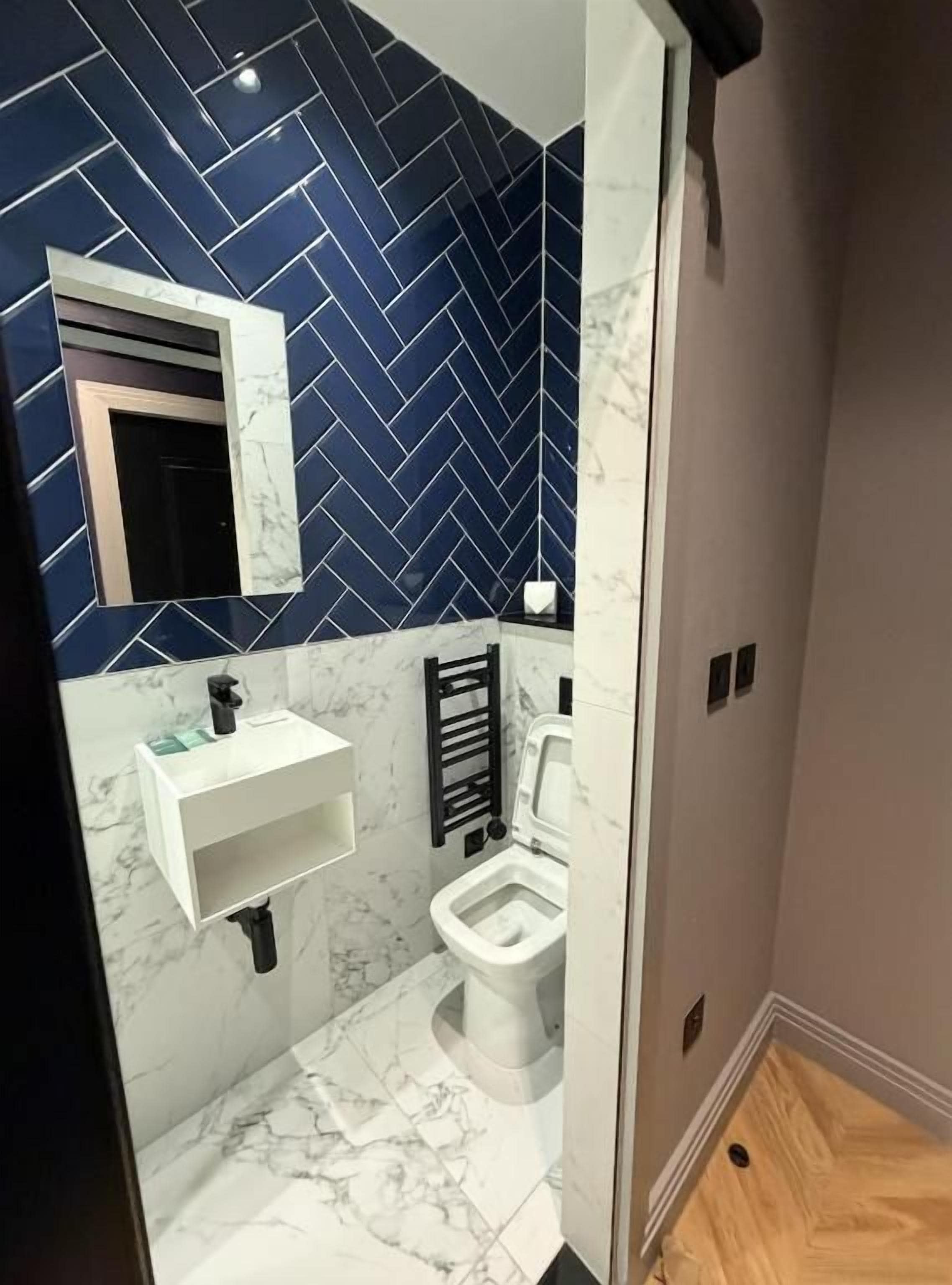 A bathroom with a herringbone-patterned wall, a white sink, a toilet, and a mirror.