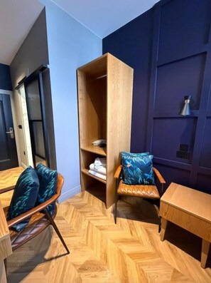 Quarto com piso em padrão herringbone, uma cadeira de madeira com almofada, uma pequena mesa de madeira e uma estante embutida de madeira com um travesseiro em cima.