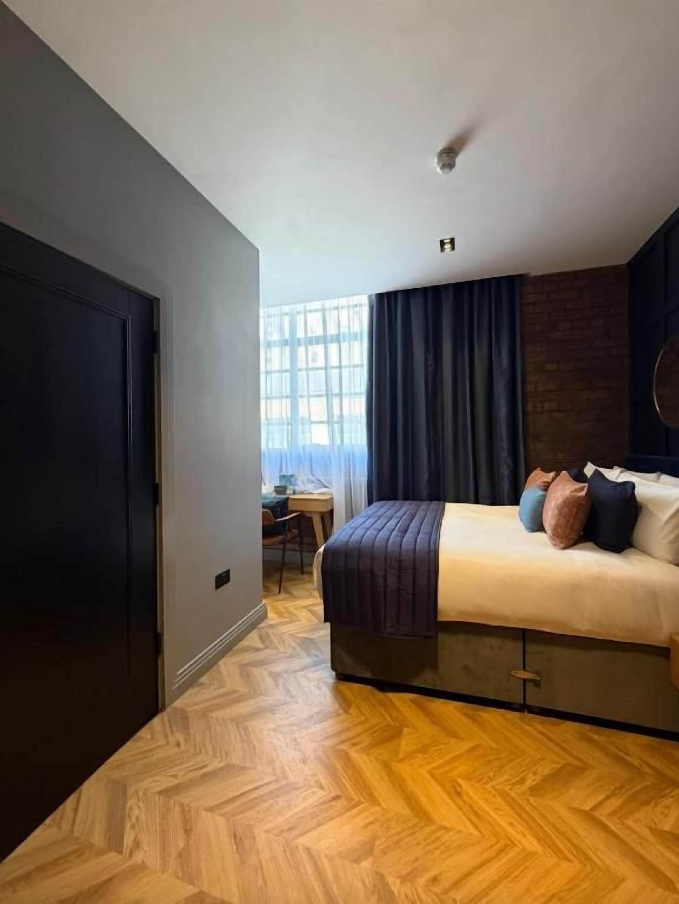 A hotel room with a bed, a desk, and a window with curtains.