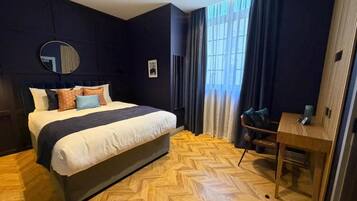 Camera d'albergo con un letto grande, una scrivania, uno specchio e una finestra con tende.