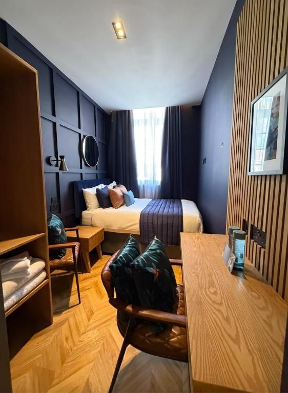 Habitación de hotel con cama, un escritorio de madera, una silla, armario y un ventanal grande.
