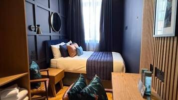 Habitación de hotel con cama, un escritorio de madera, una silla, armario y un ventanal grande.
