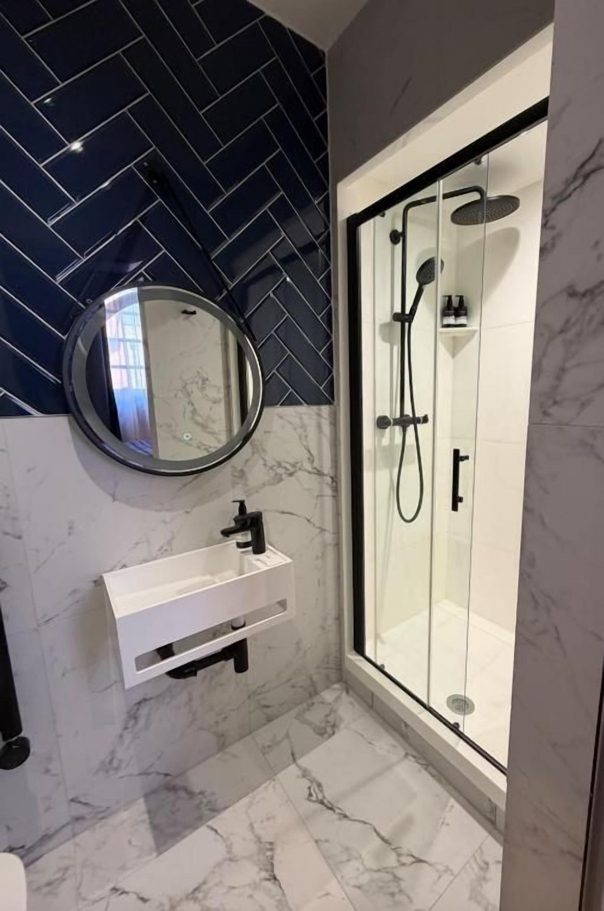 Un bagno moderno con cabina doccia in vetro, uno specchio rotondo e un pavimento in marmo.