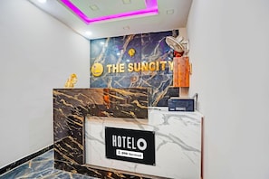 En hotelreception med en marmordisk, et skilt med 'The Suncity Hotel' og et skilt, der angiver 'Oyo-Serviced' roomservice.
